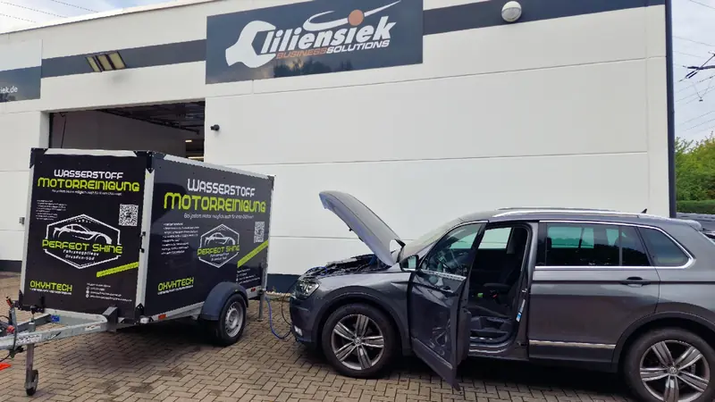 VW Tiguan mit geöffneter Motorhaube neben dem Perfect-Shine-Anhänger vor dem Autohaus Liliensiek in Dresden